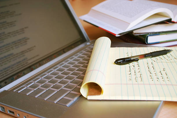 Открытый ноутбук с блокнотом, ручкой и открытыми книгами, иллюстрирующий переход к дистанционному обучению в сфере высшего образования.